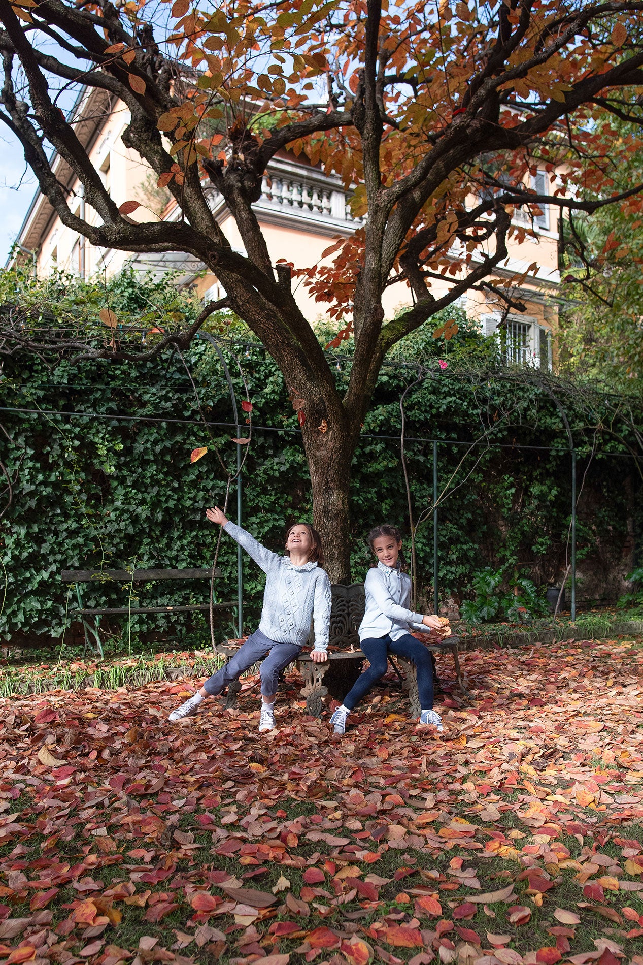 Two children playing with leaves in a garden during autumn.