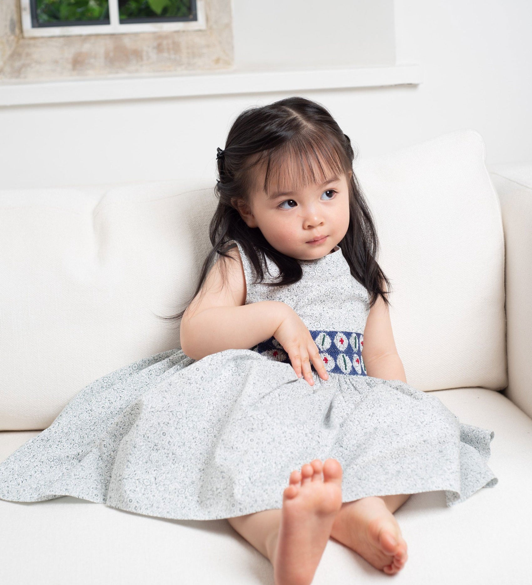 Girl wearing the Cashmirino Evelyn hand-smocked Liberty Green Flowers dress with cobalt blue embroidered waistband and teal chambray back.