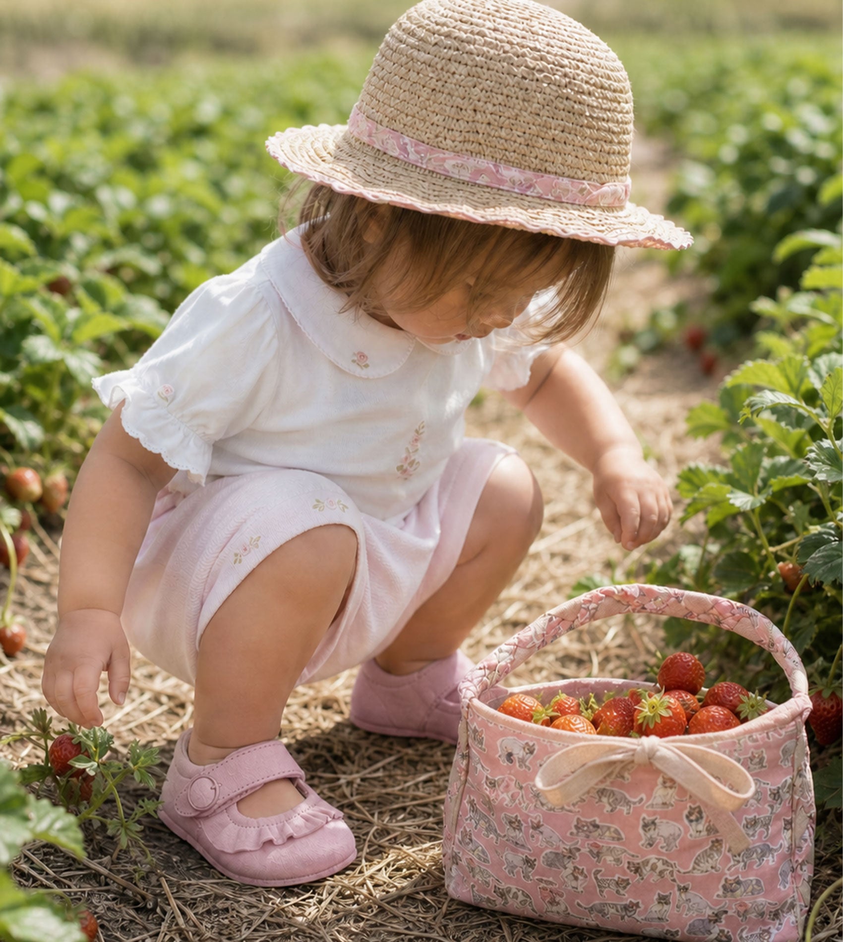 Baby girl wearing Peruvian Pima cotton bodysuit and shorts set with hand-embroidered roses picking strawberries.